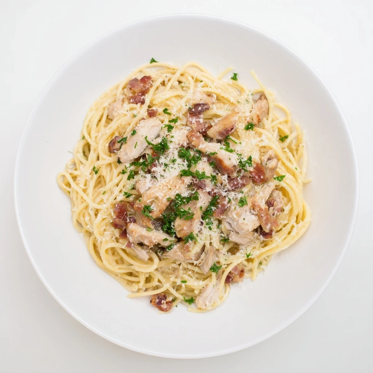 Creamy chicken carbonara served in a white bowl topped with fresh parsley and pepper.  