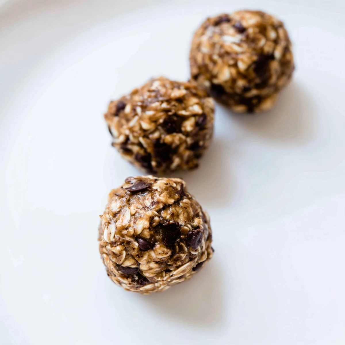 Freshly rolled Banana Chocolate Chip Energy Balls with mashed banana, oats, and chocolate chips on a wooden board.