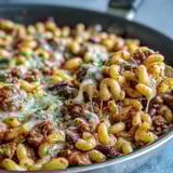 Steaming bowl of One-Pan High Protein Chili Mac topped with green onions and sour cream, served with tortilla chips on the side.