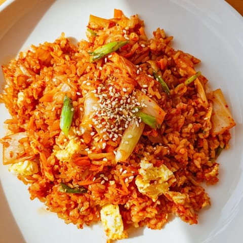 Spicy kimchi fried rice sizzles in a hot wok with caramelized kimchi, a scrambled egg, and a drizzle of toasted sesame oil.  
