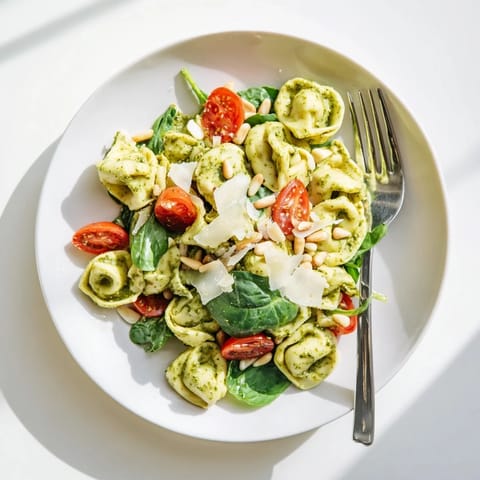 Pesto Tortellini Salad served in a white bowl, garnished with toasted pine nuts and grated Parmesan, perfect for summer picnics.  