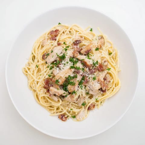 Creamy chicken carbonara served in a white bowl topped with fresh parsley and pepper.  