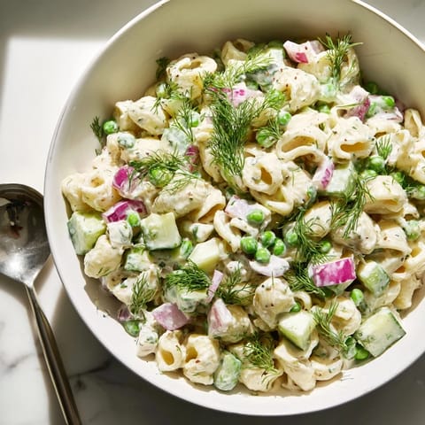 Tangy dill pickle pasta salad features al dente pasta, crunchy vegetables, and fresh dill, served chilled in a white bowl.