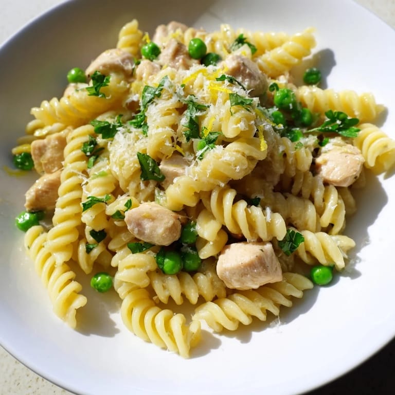 Garlic Butter Chicken & Pea Pasta is plated in a white bowl, garnished with fresh parsley and lemon zest, steam rising from the creamy, cheesy pasta.