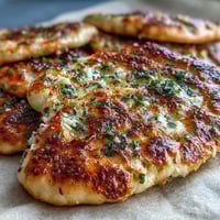 Freshly baked The Best Easy Garlic Naan Bread topped with melted butter and minced garlic.